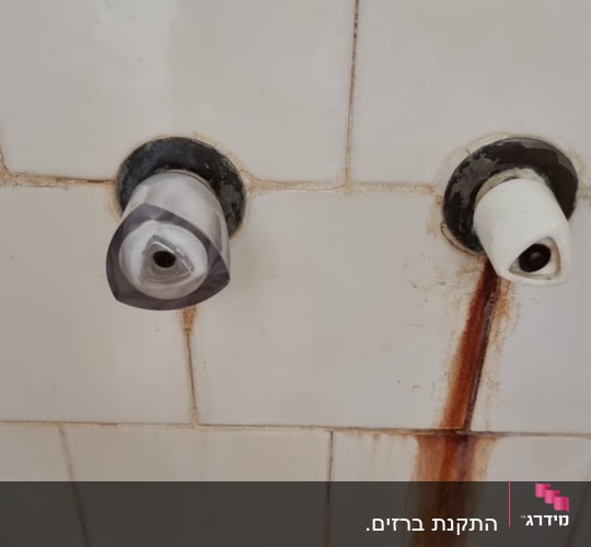ברזים ישנים עם חלודה על קיר אריחים